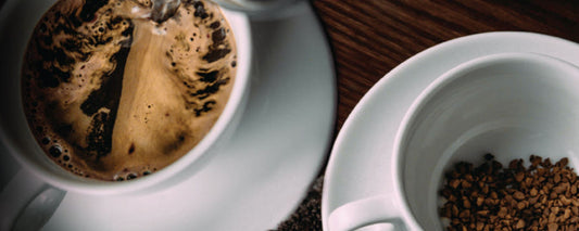 Two white cups on a wooden surface, with the left showing a swirl of dissolving instant coffee as water is poured, and the right cup filled with dry coffee granules.
