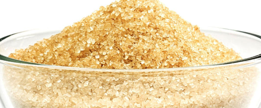 A close-up view of a glass bowl filled with coarse, golden-brown turbinado sugar, showcasing its natural crystal texture.