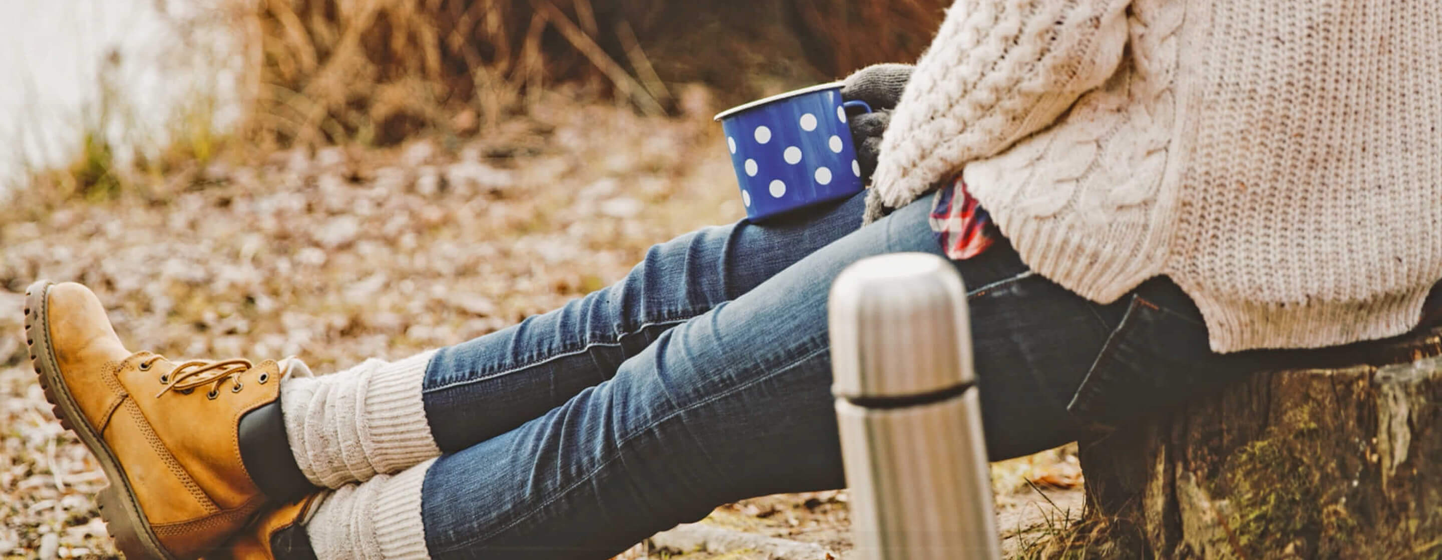 Person in cozy fall sweater holding a warm mug outdoors, enjoying coffee on a brisk autumn day.