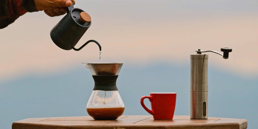 Pour-over coffee brewing with hand grinder and mug, showing café-quality preparation at home.
