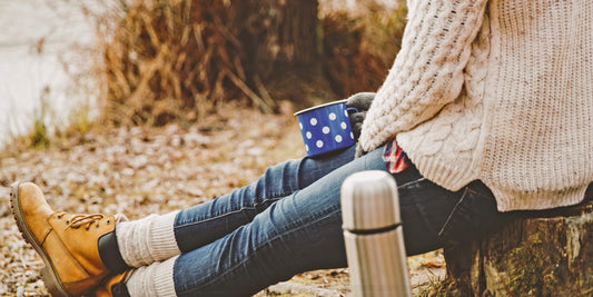 Person in cozy fall sweater holding a warm mug outdoors, enjoying coffee on a brisk autumn day.