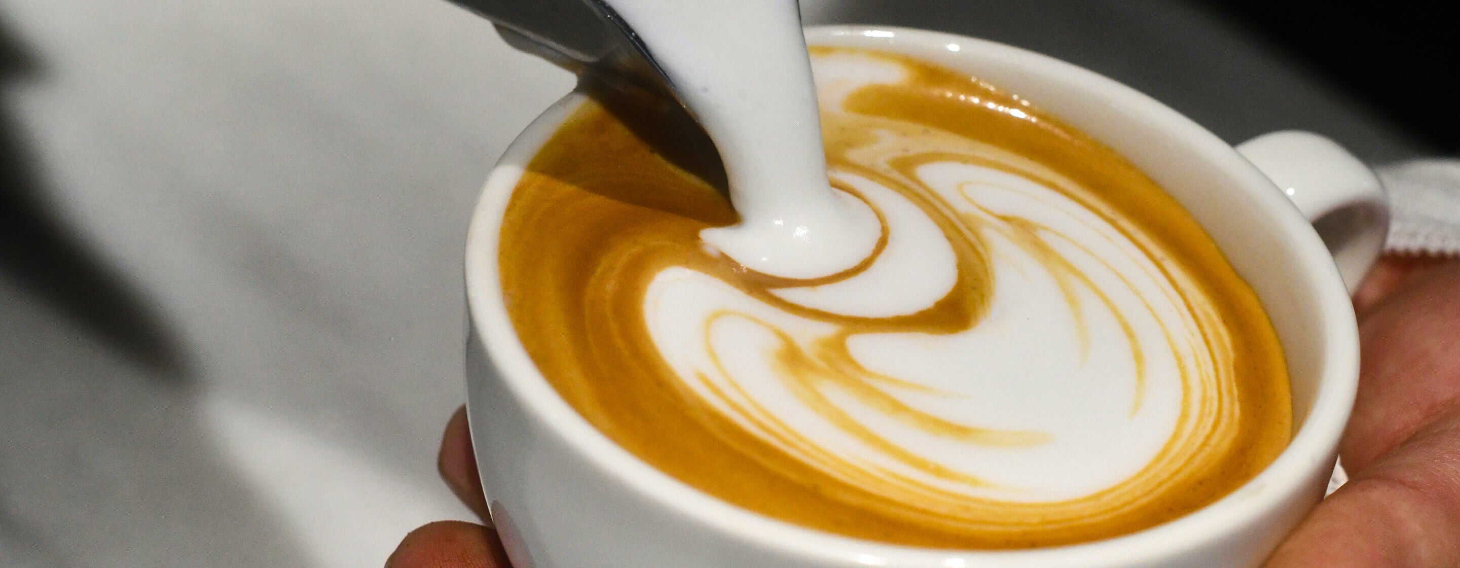 Barista pouring steamed milk into espresso to create Espresso Virtuoso latte art.